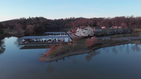 Imágenes-Aéreas-De-Drones-Sobre-El-Lago-Volando-Hacia-Un-Punto-De-Tierra-Con-Bonitas-Casas-Y-Muelles-Junto-A-Ellos-Al-Atardecer