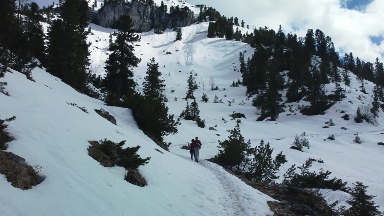 Due persone, un uomo e una donna, fanno escursioni lungo un epico sentiero panoramico di montagna innevata, in alto sopra lo scenografico Castello di Elmau in Baviera e le cime dei ghiacciai, nelle Alpi bavaresi e austriache, in una giornata nuvolosa e soleggiata nella natura.