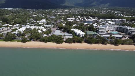 4k aerial view of a beautiful sandy beach with a small seaside town and luxury hotels in north queensland, australia