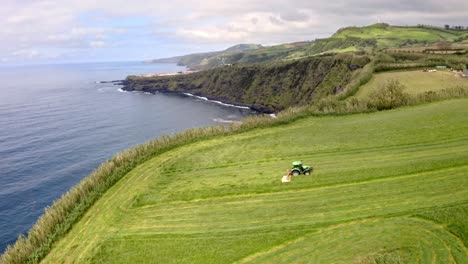 tractor cutting grass in coastal countryside, azores, aerial view