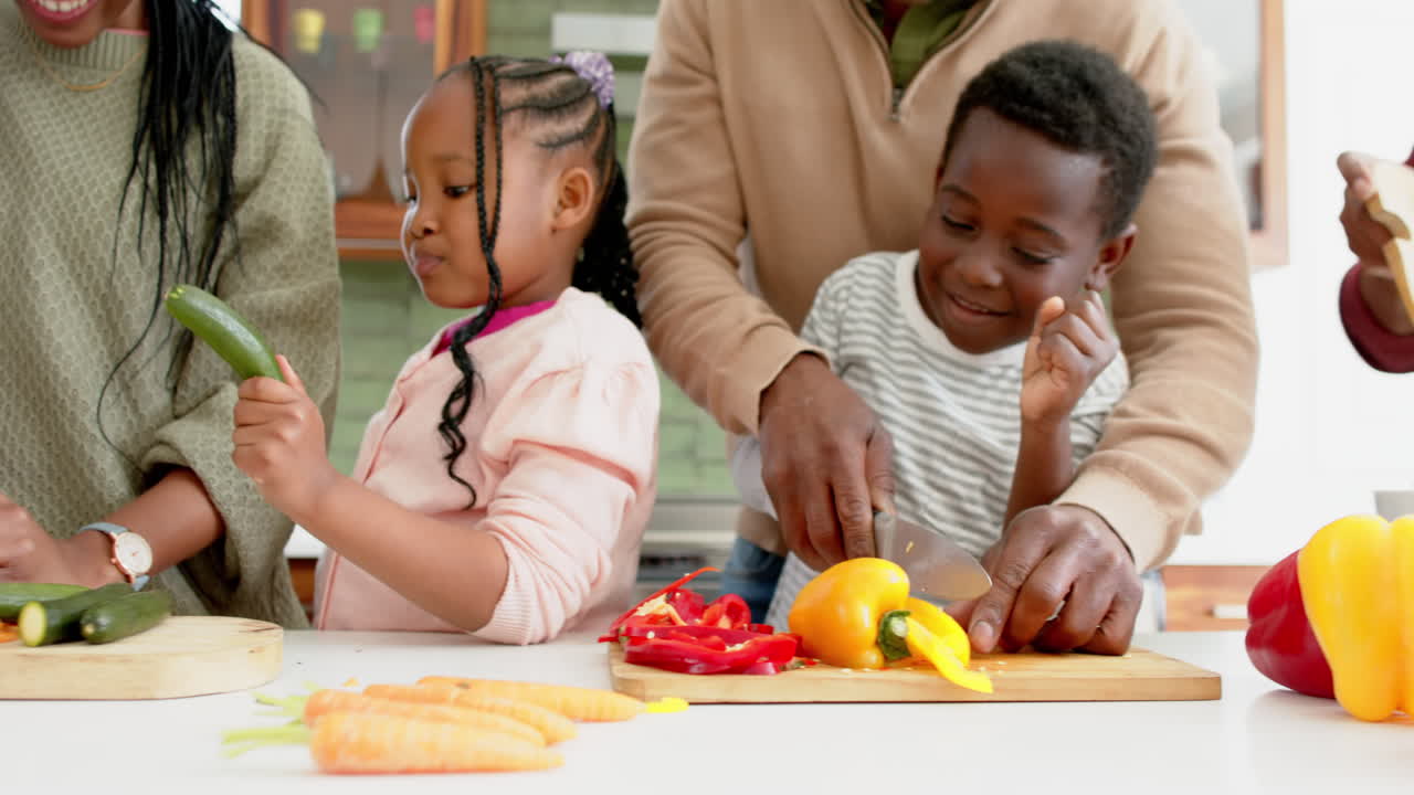 Genitori e figli afroamericani felici che tagliano verdure in cucina, al rallentatore.