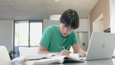 Teenage-Asian-boy-studying-intently-on-his-laptop-at-a-table