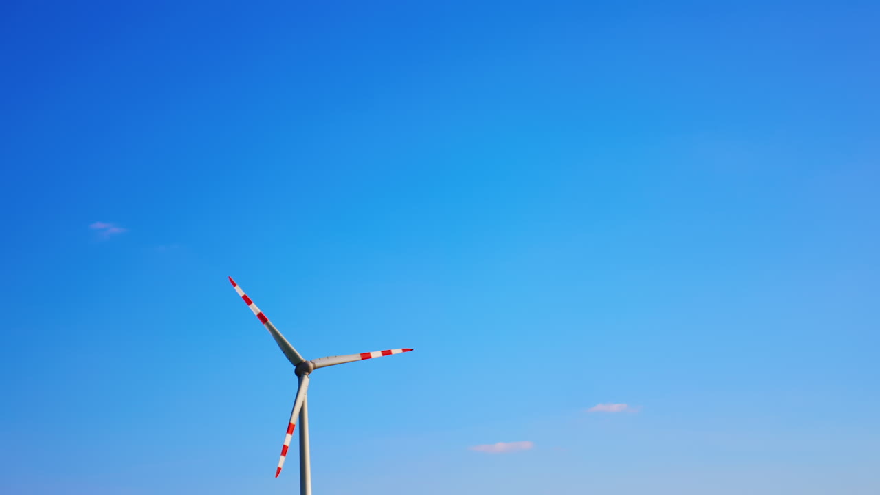 Wind turbine with red lines rotate in the blue sky. Generating green energy. Low angle view.