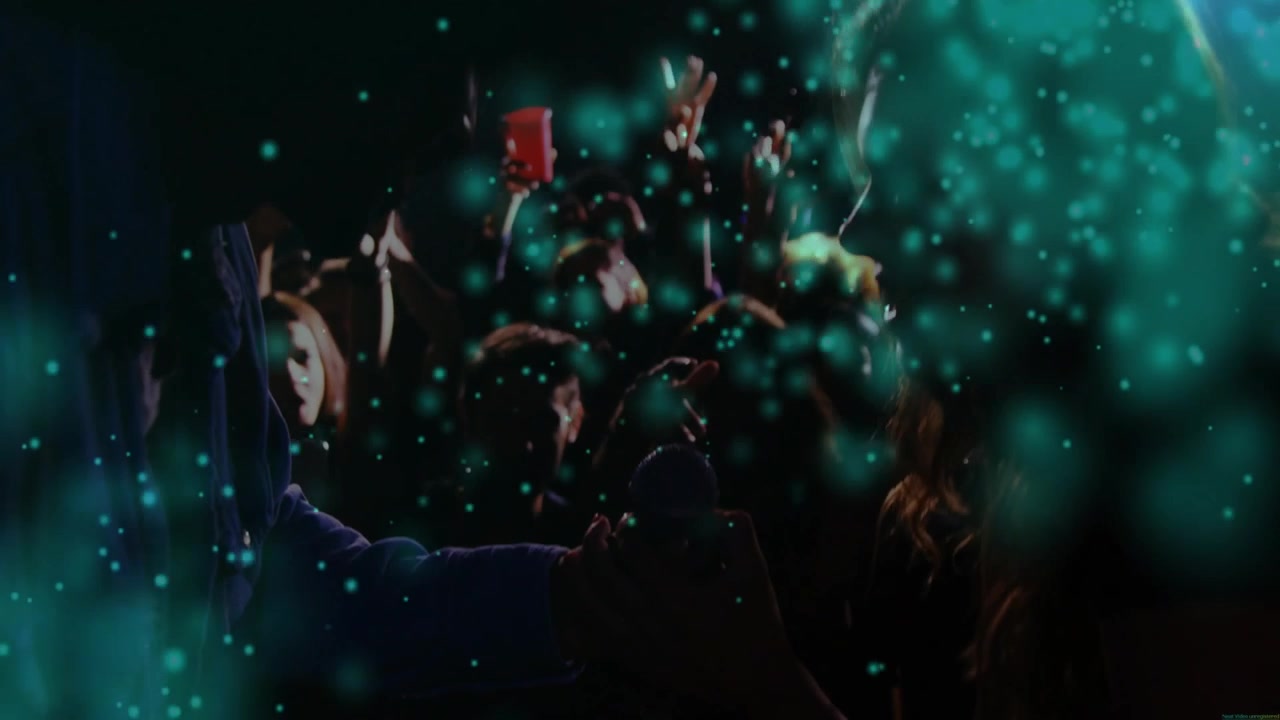 Showing front hand holding round object at dim venue, crowd raising hands, red cup, teal particles