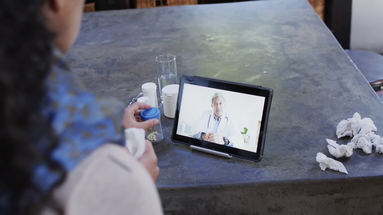 Kobieta o mieszanym pochodzeniu z przeziębieniem prowadząca rozmowę wideo za pomocą tabletu w domu, zwolnione tempo.