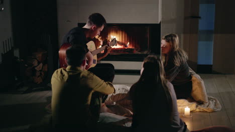 friends gather around a fireplace and play guitar