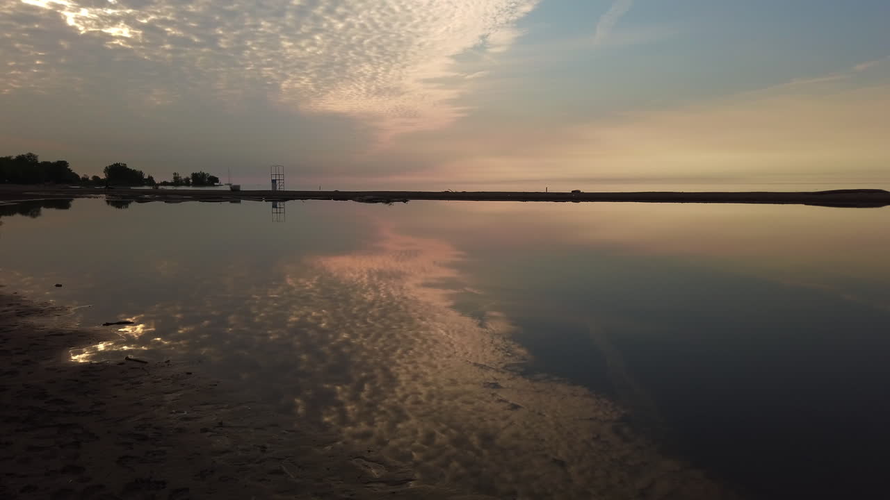 Early summer morning view of a flooded Woodbine Beach, with big sky reflecting on a calm water surface, wide shot