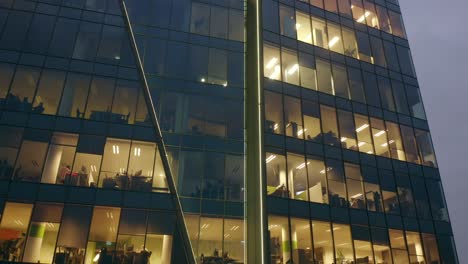 cinematic view from a drone of a night skyscraper with office windows and business people working at computers late at night.