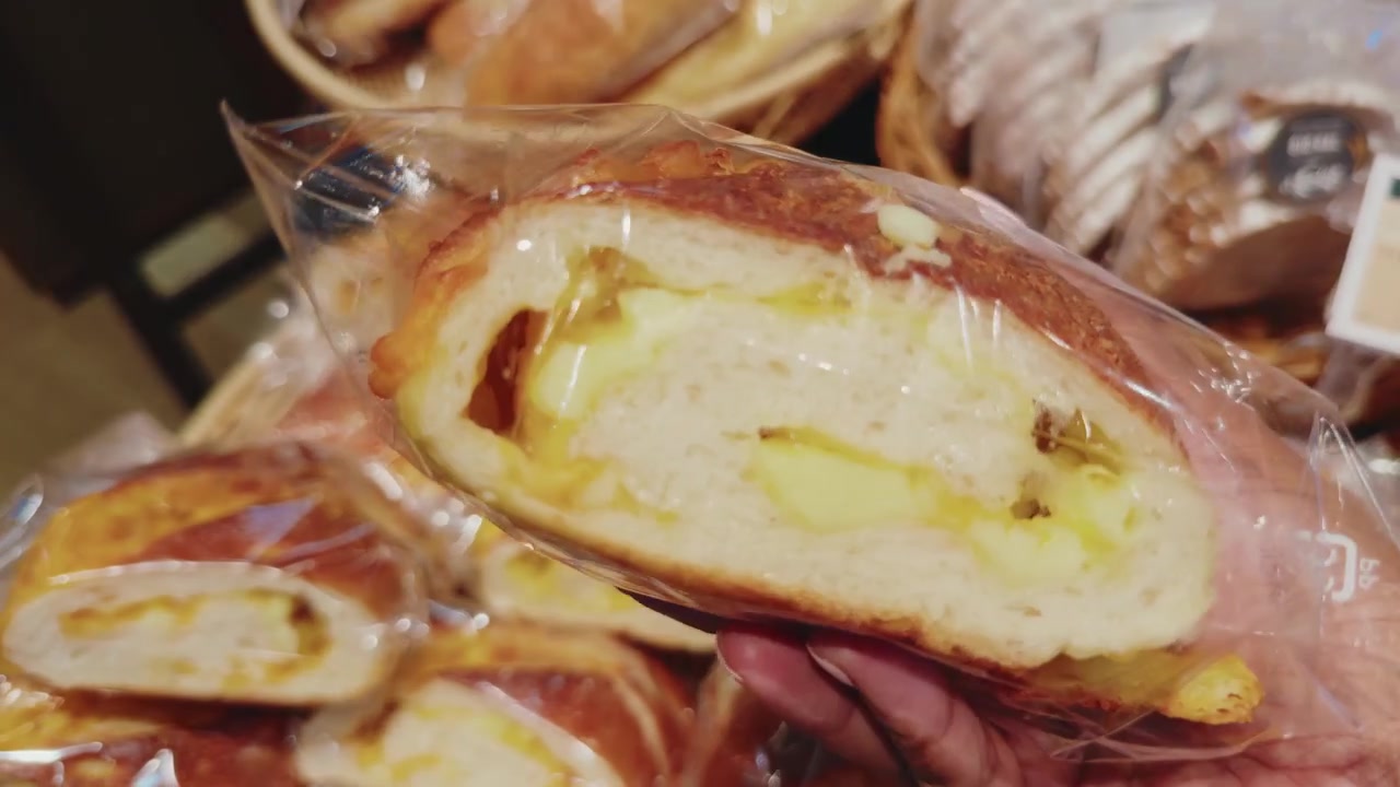 Primo piano di un cliente che prende del pane al formaggio confezionato da un banco fresco di panetteria all'interno di un supermercato, che mostra la spesa quotidiana e la scelta dei prodotti alimentari