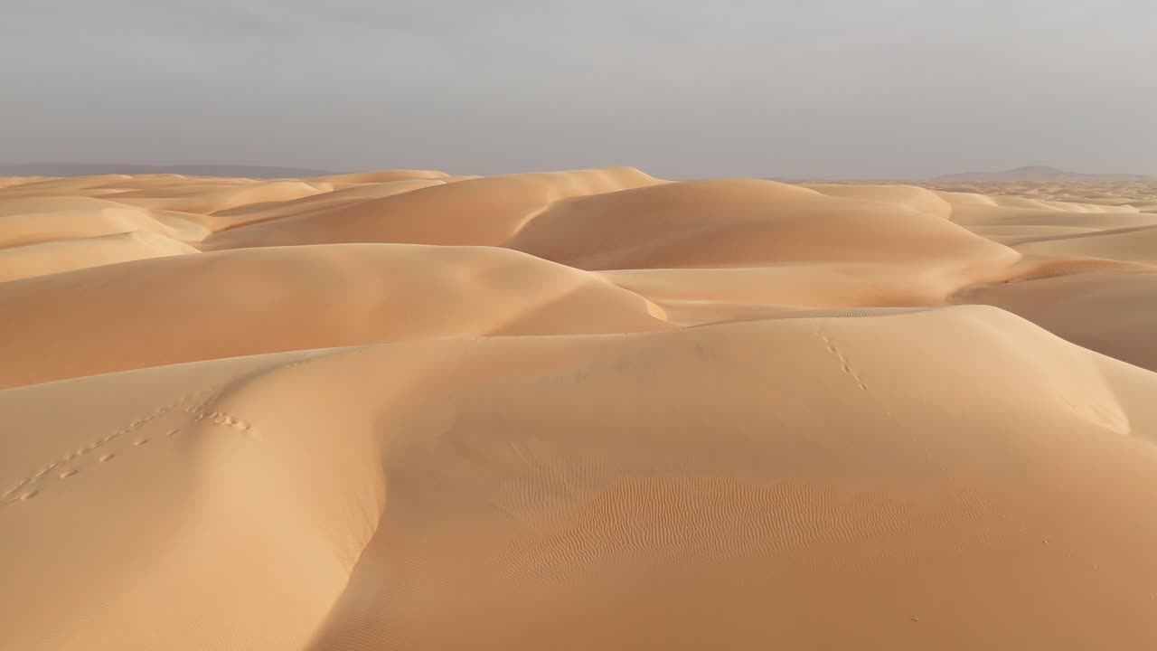 drone reveals Azouiega golden sand dunes desert soft curves, rippling patterns, dramatic sunlight and vast untouched Sahara wilderness
