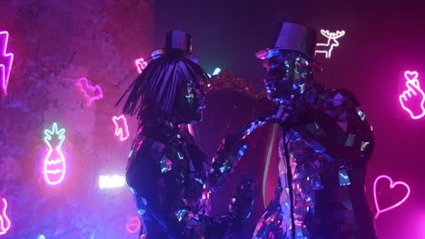 Two-robot-dancers-in-glittering-costumes-dance-against-a-neon-wall-drawing-closer-to-each-other.