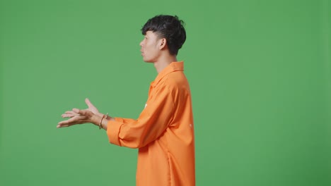 side view of wondering asian male prisoner in handcuffs standing doubtfully on the green screen background, raising hands in anger and shouting why