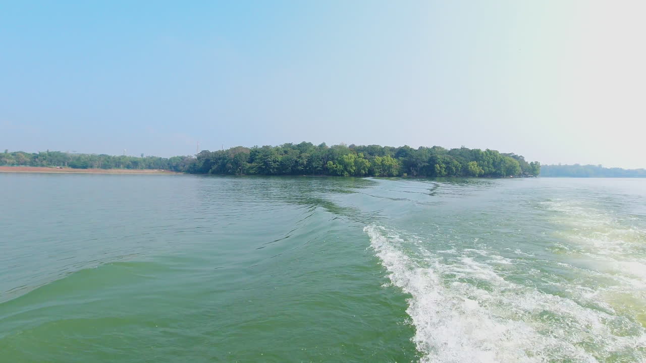 Slow motion view of distant Nagarahole forest shoreline along the Kabini River, water trail behind a boat. Karnataka, India.