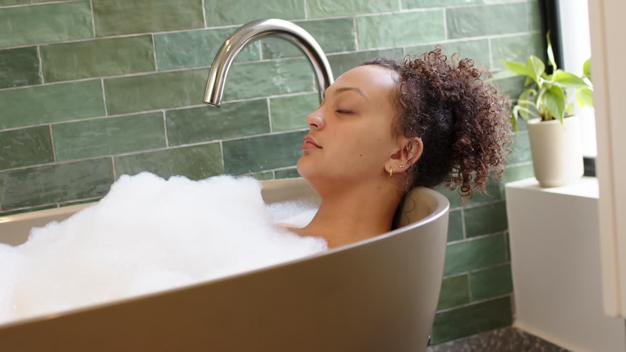 African American woman reclining in bathroom, resting in bubble foam on headrest after shift
