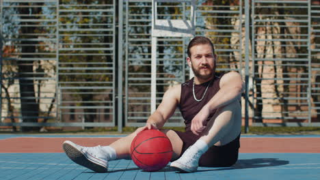 tired athletic lebanese man in sportswear relaxing after playing basketball game listening music