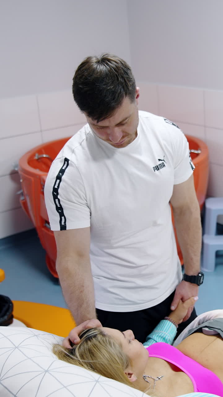 Caring husband holding hand of his wife lying in hospital bed. Man tries to sooth woman going through contractions. Top view. Vertical video