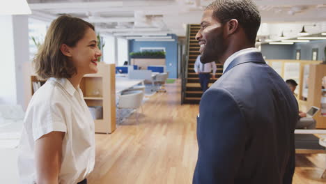 Two-Businesswoman-And-Businessman-Meet-And-Shake-Hands-In-Modern-Open-Plan-Office