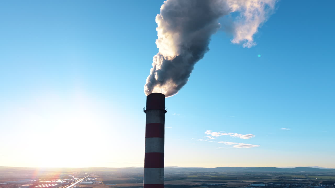 Ciminiera industriale a strisce rosse e bianche che emette fumo bianco. Primo piano di un'alta ciminiera industriale con strisce rosse e bianche che rilascia vapore o fumo su sfondo di cielo blu.
