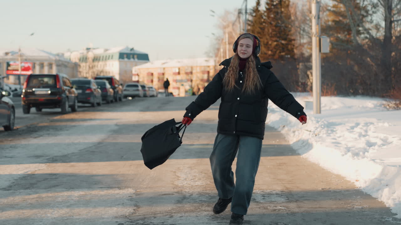 Donna che passeggia in una giornata invernale. Una signora in abiti invernali cammina tra veicoli parcheggiati al mattino presto. Una donna vestita caldamente con un berretto si muove per una strada urbana innevata all'alba.