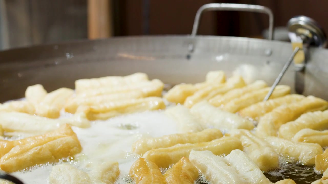 Primo piano di bastoncini di pasta dorati che friggono in olio bollente all'interno di un grande wok di metallo.