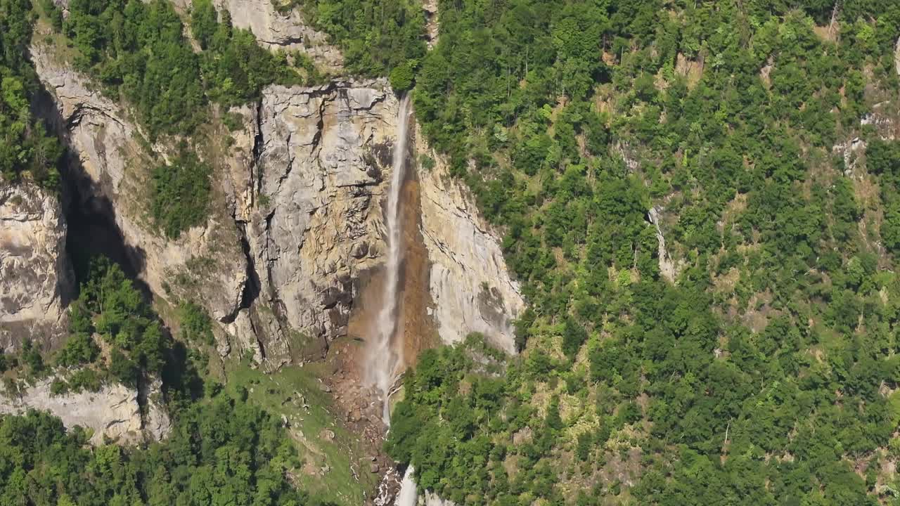 Aerial drone view revealing the Seerenbachfälle waterfalls cascading down steep cliffs surrounded by dense green forest in Amden, Switzerland