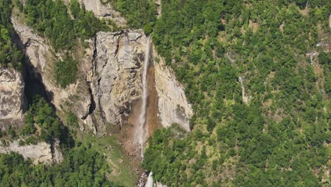 aerial drone view revealing the seerenbachfälle waterfalls cascading down steep cliffs surrounded by dense green forest in amden, switzerland