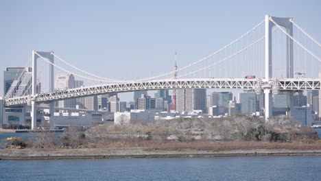 vehicles driving across rainbow bridge over tokyo bay with tokyo tower and skyline in background