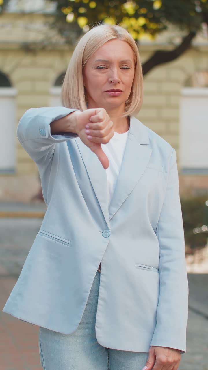 Upset mature caucasian blonde businesswoman in formal suit looking camera and showing thumb down