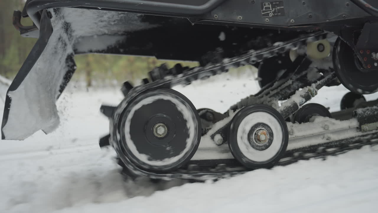 Atv track spins through packed snow, dynamic closeup of rollers and drive sprocket biting powder, ice buildup and snow spray, fast rotation showing torque and power, pine forest backdrop, gritty