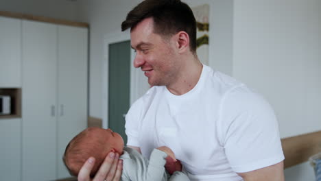 caucasian man in white t-shirt waving his newborn baby. happy father dandling his little son in maternity hospital.