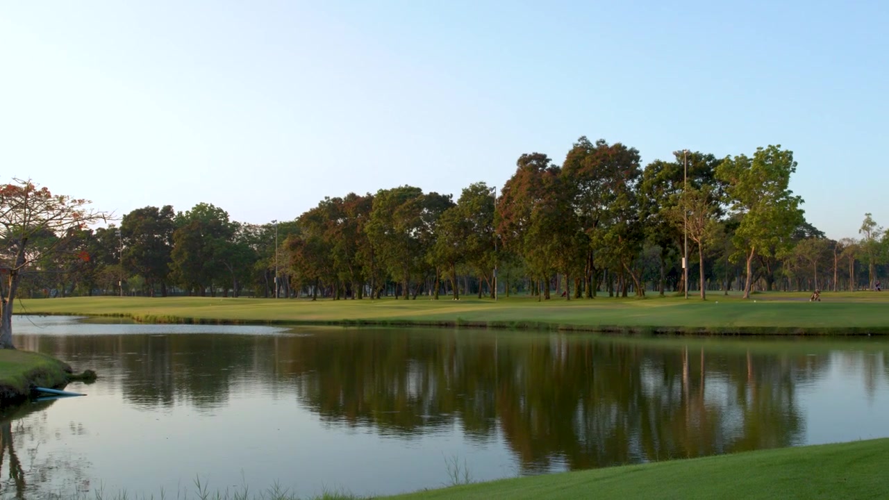 Bidikan Panning Lebar Fairway Lapangan Golf Hijau di Samping Danau Tenang yang Memantulkan Cahaya