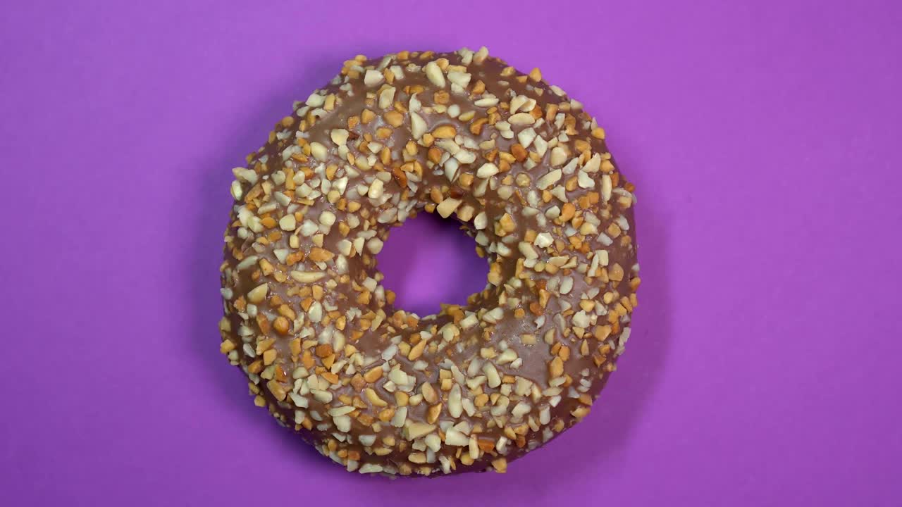 Chocolate sweet donut rotating on a plate. Top view. Purple background.