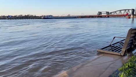 strong current and calm waves reaching bench on the countenance boulevard hit by water during winter high level of river ijssel showing partly flooded boulevard