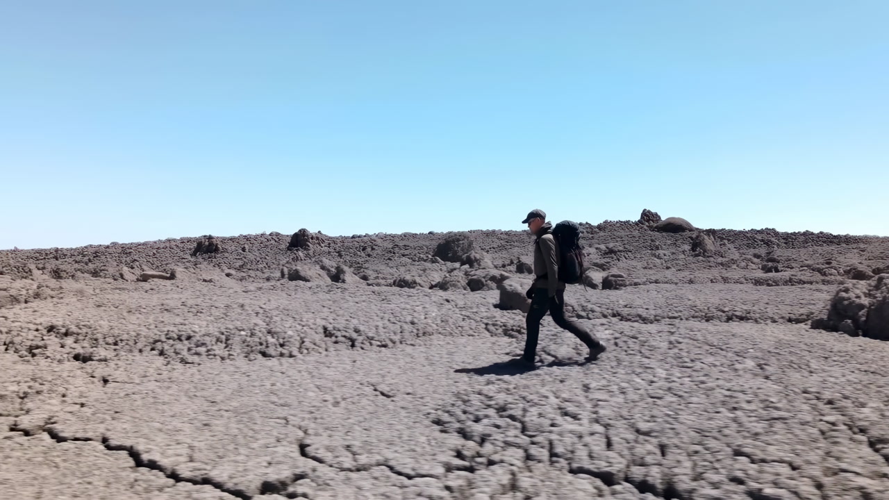 Solitary Hiker Crossing Cracked Volcanic Plain, Backpacked Traveler Walking Across Barren Rocky Terrain