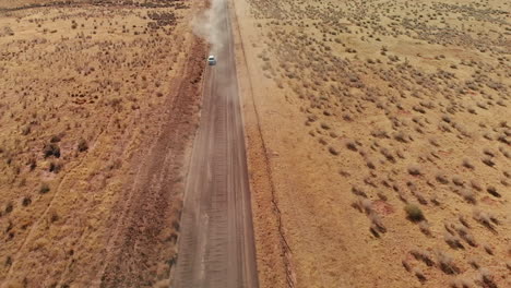 Small-White-Car-with-Bike-Rack-on-Dusty-Desert-Road,-Aerial
