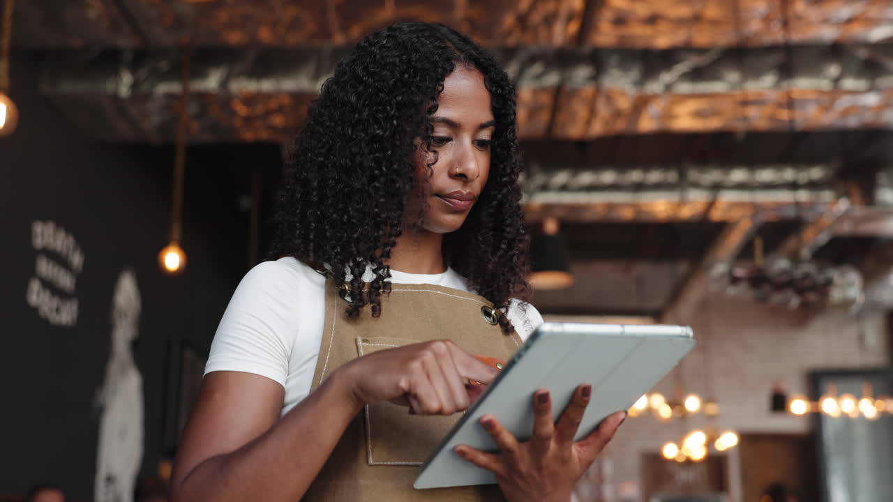 Young Black Woman in Apron Using Digital Tablet in Cafe