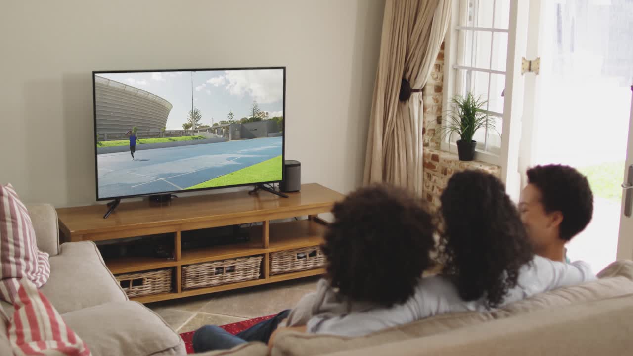 Composizione di famiglia felice seduta insieme a casa che guarda un evento di atletica leggera di lancio del giavellotto in TV.