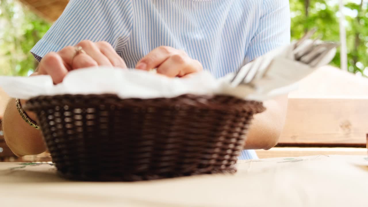 Young female picking up bread from traditional Greek bread basket outdoors
