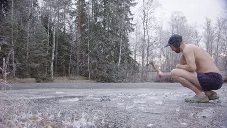 un bañista de hielo hipster entra en el marco y comienza a cortar el hielo para hacer un agujero