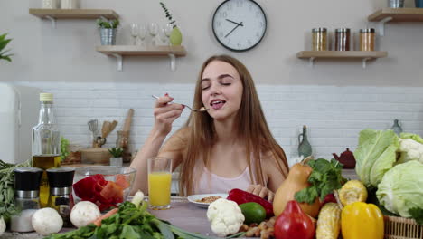 Lovely-girl-eating-raw-sprouts-buckwheat-with-nuts-in-kitchen-with-fresh-vegetables-and-fruits