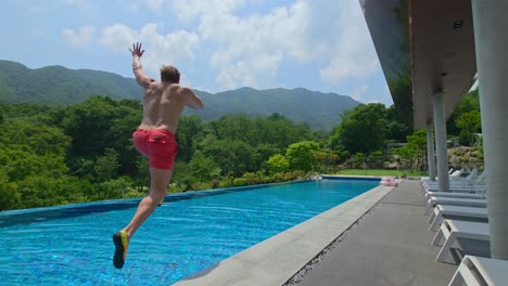 a man in his thirties enjoys his summer vacation by jumping into a beautiful infinity pool at a luxury hotel and mountain resort with a stunning view, celebrating freedom and fun - slow motion