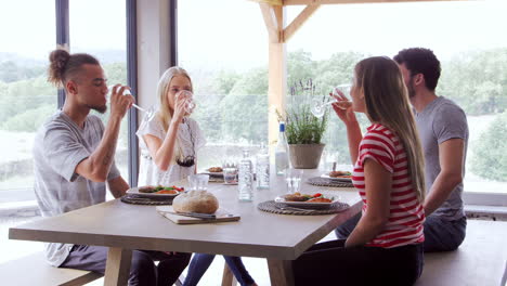 Four-young-adult-friends-celebrate,-smiling-and-raising-wine-glasses-during-a-dinner-party