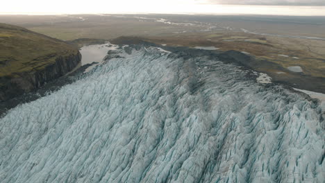 Large-glacier-in-Iceland-flowing-down-mountain-to-green-plains