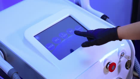 gloved cosmetologist's hand chooses the necessary parameter on the sensor screen of equipment. beautician prepares laser for usage.