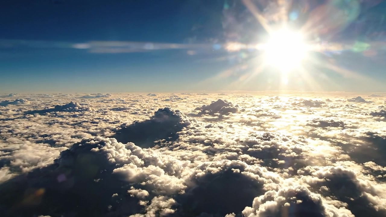 Una vista aerea mozzafiato di nuvole sotto un sole splendente, che cattura la bellezza eterea del cielo all'alba con raggi di sole luminosi che si diffondono sull'orizzonte blu