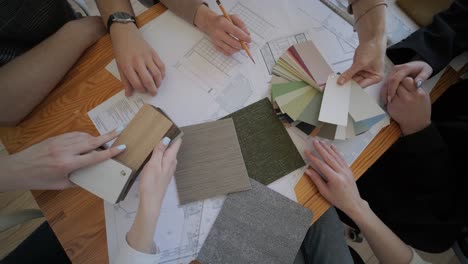 a collaborative design meeting in action, with team members selecting materials and colors, consulting floor plans, and engaging in creative decision-making for an interior design project.