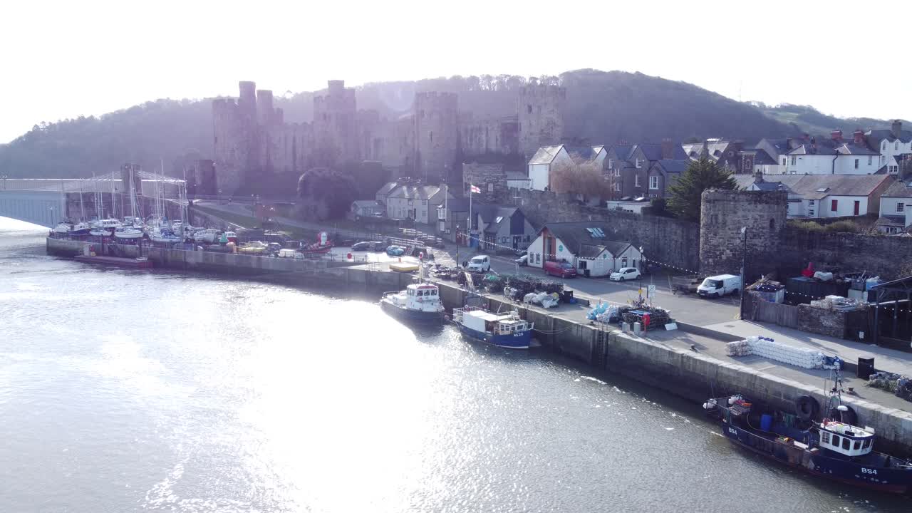 목가적인 콘위 성(conwy castle)과 항구 어촌 마을 보트가 연안 해안가에서 공중 아래로 내려가고 있습니다.