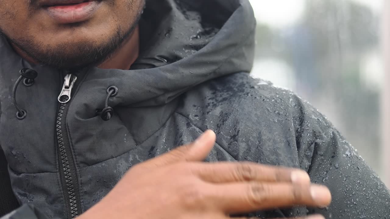 Close-up of Hand Touching Waterproof Jacket with Raindrops