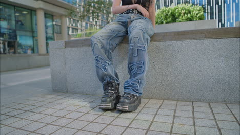 close up de moda al aire libre que muestra vaqueros y botas de jóvenes de estilo alternativo mujer con tatuajes sentada fuera de edificios modernos filmada en tiempo real