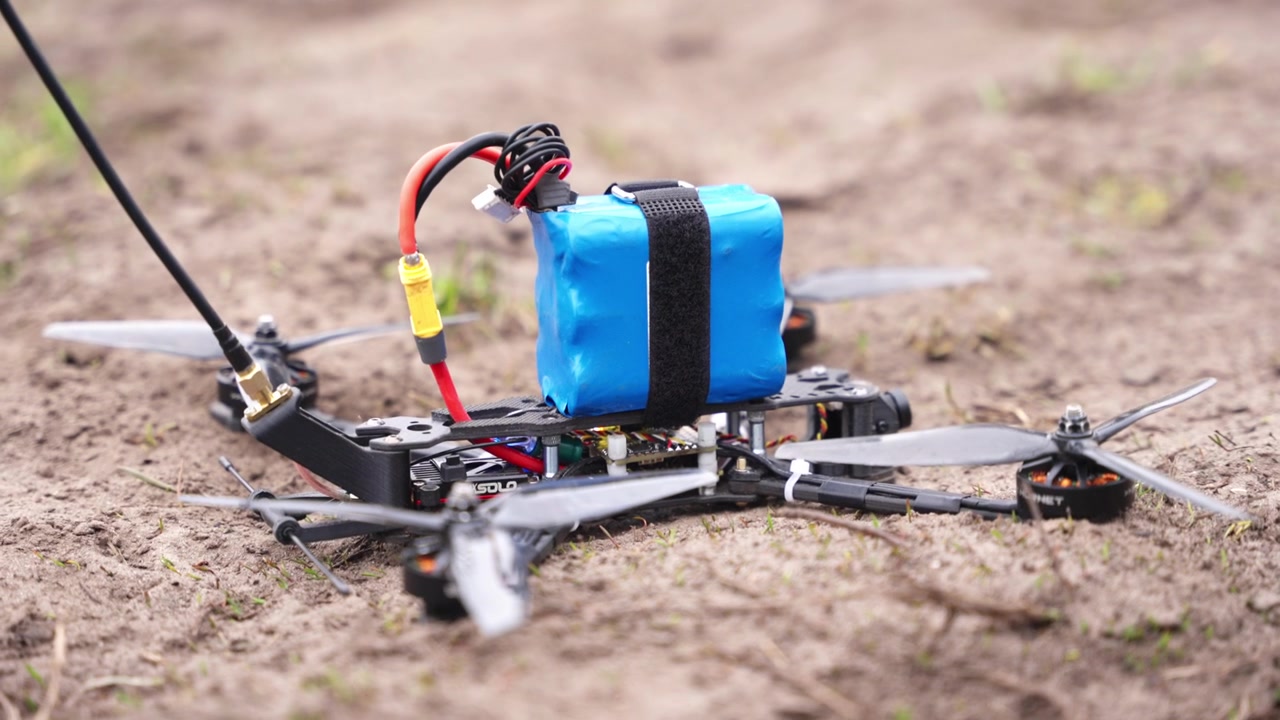 Close of FPV drone on ground with battery pack and wiring visible in outdoor setting